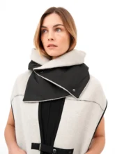 The model is shown with the hood up on the grey wool pocket scarf, accentuating the black collar and white-bordered pockets, in an industrial backdrop.