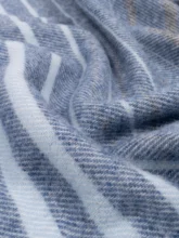 A luxurious grey recycled wool blanket with a plush texture and elegant blue stripes, captured in a close-up to emphasize its cozy weave.