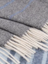 Folded edge of a grey recycled wool blanket featuring a detailed stripe design and clean white fringes, offering a look of simple sophistication.