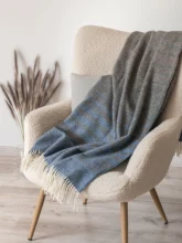 A dark recycled wool blanket gracefully draped over a cream chair, with a gentle contrast of colors that creates a warm, inviting ambiance.