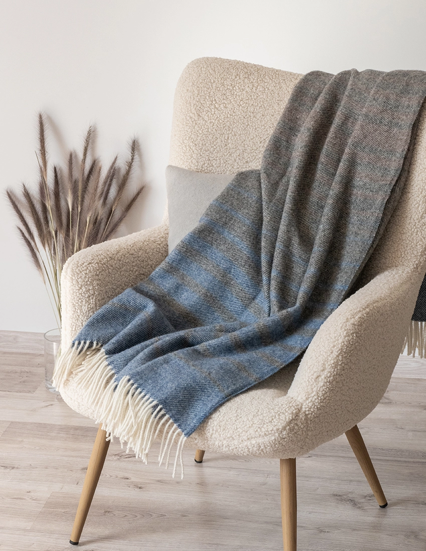 A dark recycled wool blanket gracefully draped over a cream chair, with a gentle contrast of colors that creates a warm, inviting ambiance.