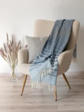 Striped recycled wool blanket casually thrown over a beige armchair, adding a touch of comfort and style to the living space.