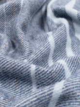 An artistic, close-up shot of a striped recycled wool blanket highlighting the texture and soft folds of the fabric in shades of blue.